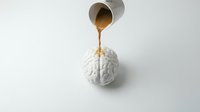 Coffee being poured from metallic cup onto white brain model representing caffeine effects on cognitive function and mental stimulation for educational use.