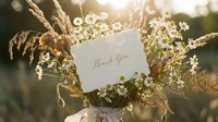 Wildflower bouquet with daisies and wheat held outdoors in golden sunlight, featuring a thank you card with elegant script lettering.