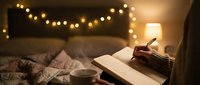 Cozy bedroom scene with open book, warm string lights above headboard, and glowing bedside lamp creating intimate reading atmosphere.