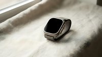 Modern smartwatch with black screen and metal band resting on textured fabric surface near window with natural lighting for technology lifestyle concepts.