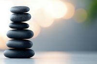 Balanced stack of smooth black zen stones on blurred background with soft bokeh lights creating peaceful spa and meditation atmosphere.