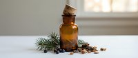 Amber glass bottle with cork stopper surrounded by pine branches, juniper berries and spices on white surface for natural aromatherapy and wellness products.