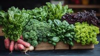 Fresh organic vegetables and greens arranged in wooden box with kale, lettuce varieties, radishes and herbs on dark rustic background. Local farm produce.