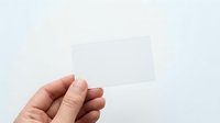 Caucasian hand holding blank white business card or paper mockup against neutral background for branding and corporate design projects.