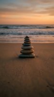 Balanced stone cairn on sandy beach at sunset with golden sky and ocean waves creating peaceful meditation scene for wellness and mindfulness concepts.