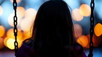 Silhouette of woman on swing against blurred bokeh lights at dusk, creating atmospheric mood for emotional storytelling.