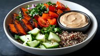 Fresh buddha bowl with grilled carrots, quinoa, cucumber, cherry tomatoes, herbs and creamy hummus sauce served in white ceramic bowl on dark background.