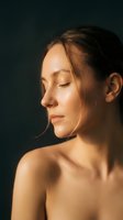 Serene young woman with closed eyes in warm golden light against dark background, peaceful meditation and mindfulness concept for wellness and self-care.