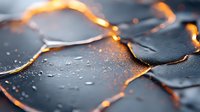 Shattered glass fragments with glowing orange edges on dark background with water droplets create dramatic contrast and mysterious atmosphere.