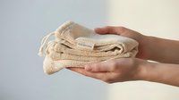 Hands holding folded reusable cotton mesh produce bags for zero waste shopping and sustainable lifestyle choices.