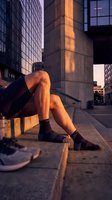 Athletic woman legs in black socks sitting on urban concrete steps during golden hour sunset with modern city buildings in background for fitness lifestyle.