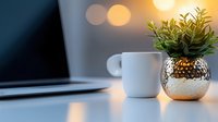 Small green plant in decorative metallic pot on modern desk with laptop and warm bokeh lights creating cozy workspace atmosphere for productivity.