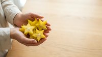 Unrecognizable person holding fresh yellow star fruit slices in palm against wooden surface, healthy eating and nutrition concept.