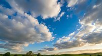 Dramatic blue sky with fluffy white clouds over rural landscape at sunset. Natural outdoor scenery with expansive horizon and golden light for backgrounds.