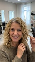 Smiling middle-aged Caucasian woman with curly blonde hair in modern hair salon touching her styled curls after professional treatment.