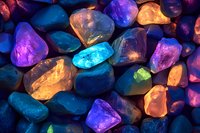 Glowing colorful mineral crystals and stones in vibrant neon colors of blue, purple, orange and green on dark background, illuminated from within creating magical effect.
