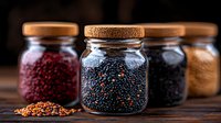 Glass jars filled with colorful grains and seeds including black quinoa, red quinoa and spices on rustic wooden table, selective focus on center jar for food background.