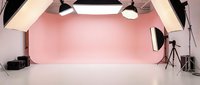 Professional photography studio setup with pink backdrop wall and white floor. Studio lighting equipment, softboxes, and tripods ready for commercial shoots.
