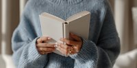 Person in cozy blue sweater holding open book with blank pages, perfect for education, reading, or literary concepts.