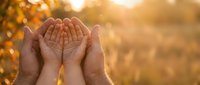 Open cupped hands reaching toward golden sunlight in warm autumn setting, symbolizing hope, prayer, gratitude and spiritual connection with nature's blessing.