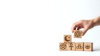 Hand placing wooden blocks with religious symbols including cross, star of David, crescent moon, ankh and eye representing diverse faiths and spirituality.