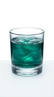 Glass of turquoise liquid with ice cubes and splashing water isolated on white background, suitable for beverage, drink, and refreshment design projects.
