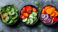 Fresh colorful vegetable bowls with spinach, tomatoes, cucumber slices, carrots and red onion rings on dark background, healthy eating concept.