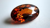Oval cut deep red garnet gemstone with brilliant facets and rich amber undertones on white background, showcasing natural crystal clarity and luxurious sparkle.