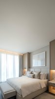 Luxury bedroom interior with neutral tones, upholstered headboard, white bedding, decorative pillows, framed artwork, sheer curtains, and warm ambient lighting for hospitality design.