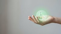 Caucasian hand holding glowing green wheelchair accessibility icon, symbolizing disability support, inclusive care, and social responsibility for healthcare and community services.