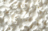 Creamy white whipped texture with tiny golden speckles creates soft peaks and valleys, macro photography showing delicate food surface details and light shadows.