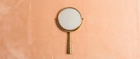 Vintage brass magnifying glass with round lens on textured peach wall background, suitable for detective, research, and educational design projects.