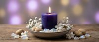 Purple candle burning on wooden plate with white pebbles and baby's breath flowers. Spa relaxation aromatherapy meditation wellness concept with bokeh lights.