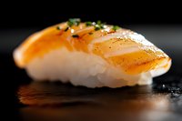 Fresh salmon nigiri sushi with rice garnished with green onions and black pepper on dark background, close-up macro shot with selective focus and reflection.