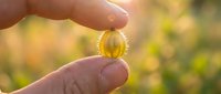 Closeup of hand holding golden capsule supplement against blurred natural background, representing wellness and nutritional health products for medical and lifestyle content.