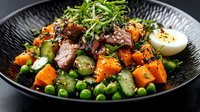 Asian-inspired salad with tender duck meat, roasted sweet potato cubes, green peas, cucumber slices, soft-boiled egg and fresh microgreens on black plate.