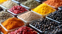 Vibrant array of colorful ground spices and peppercorns in square bowls including turmeric, paprika, black pepper, pink peppercorns and aromatic seasonings for cooking.