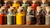 Colorful spices and herbs in glass jars with cork lids arranged on wooden shelf for cooking, seasoning, culinary arts and kitchen organization.