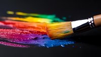 Paint brush with colorful rainbow pigments smeared on dark surface, showing vibrant artistic strokes and creative expression in macro photography.
