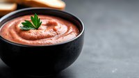 Creamy pink sauce in black ceramic bowl garnished with fresh parsley leaf, served on dark concrete background with selective focus and copy space.