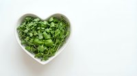 Fresh green microgreens in heart-shaped bowl on white background. Healthy organic sprouts for salads, smoothies and nutritious meals. Clean eating concept.