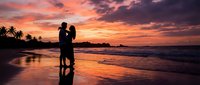 Romantic couple silhouette embracing on tropical beach at sunset with dramatic orange and pink sky reflecting on wet sand and palm trees in background.