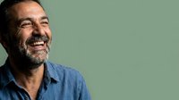 Middle-aged man with dark beard wearing blue shirt smiling against green background, suitable for corporate portraits and business communications.