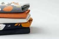 Stack of folded cotton and linen fabrics in orange, gray and white colors with floral pattern on white background. Modern textile design for home decor.