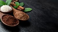 Wooden spoons with cocoa and coconut powder on dark stone background with mint leaves and cinnamon sticks, culinary ingredients for baking and desserts.