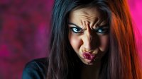 Young woman with intense expression against vibrant pink background, dramatic lighting creating contrast on face with colorful highlights in dark hair.