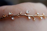 Delicate gold branch ring with crystal leaves wrapped around finger, featuring dainty clear stones in floral design against soft skin background.