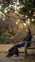 Professional businesswoman in dark suit sitting on wooden park bench during golden hour autumn evening with warm bokeh lighting for corporate lifestyle.