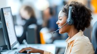 Young African American female customer service representative wearing headset while working at computer in modern call center office environment.