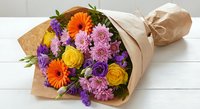 Colorful mixed flower bouquet with yellow roses, orange gerberas and purple chrysanthemums wrapped in kraft paper on white wooden background for gifts.